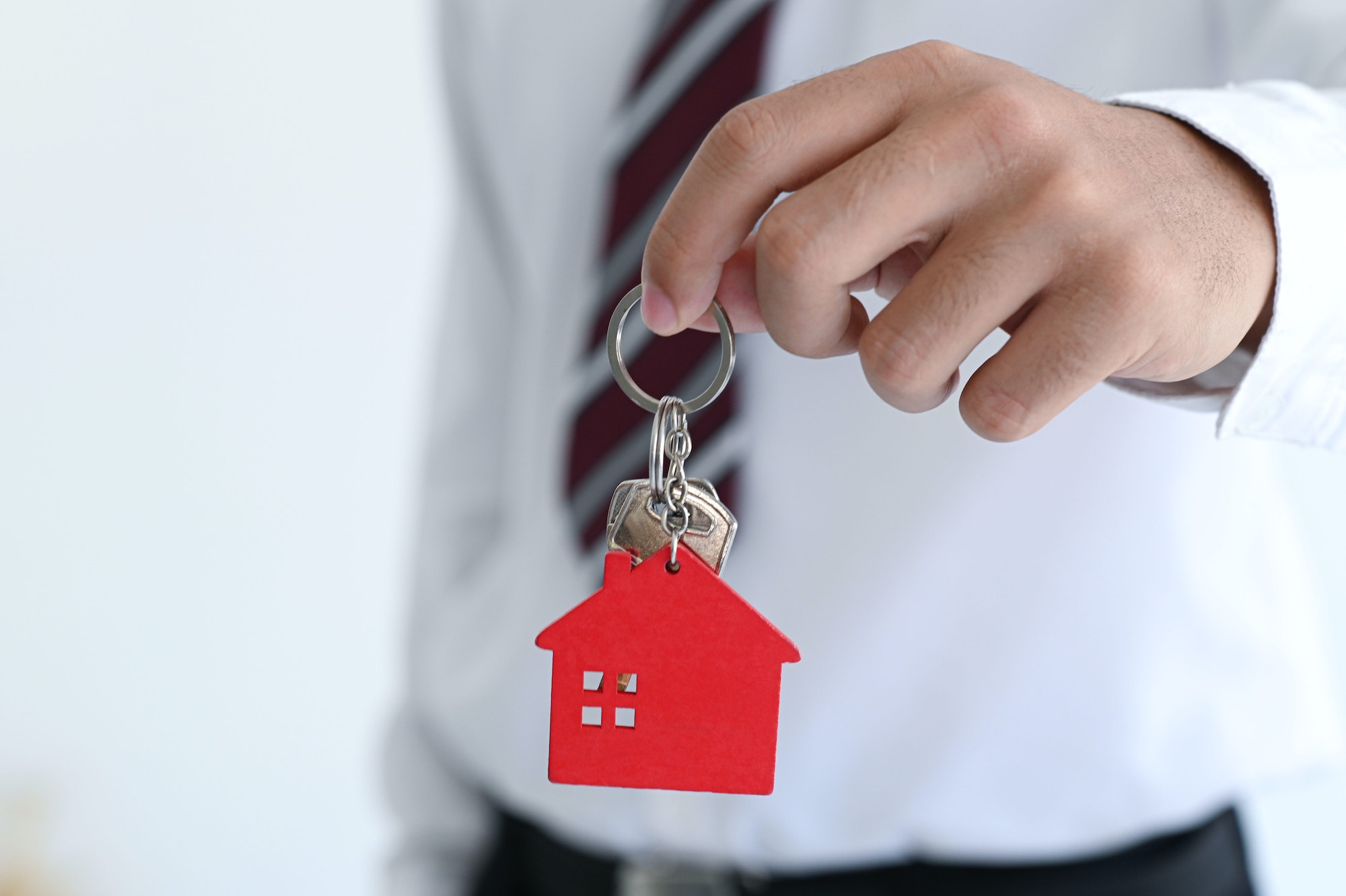 Male hand holding a keychain with model house, real estate trading concept, real estate insurance.